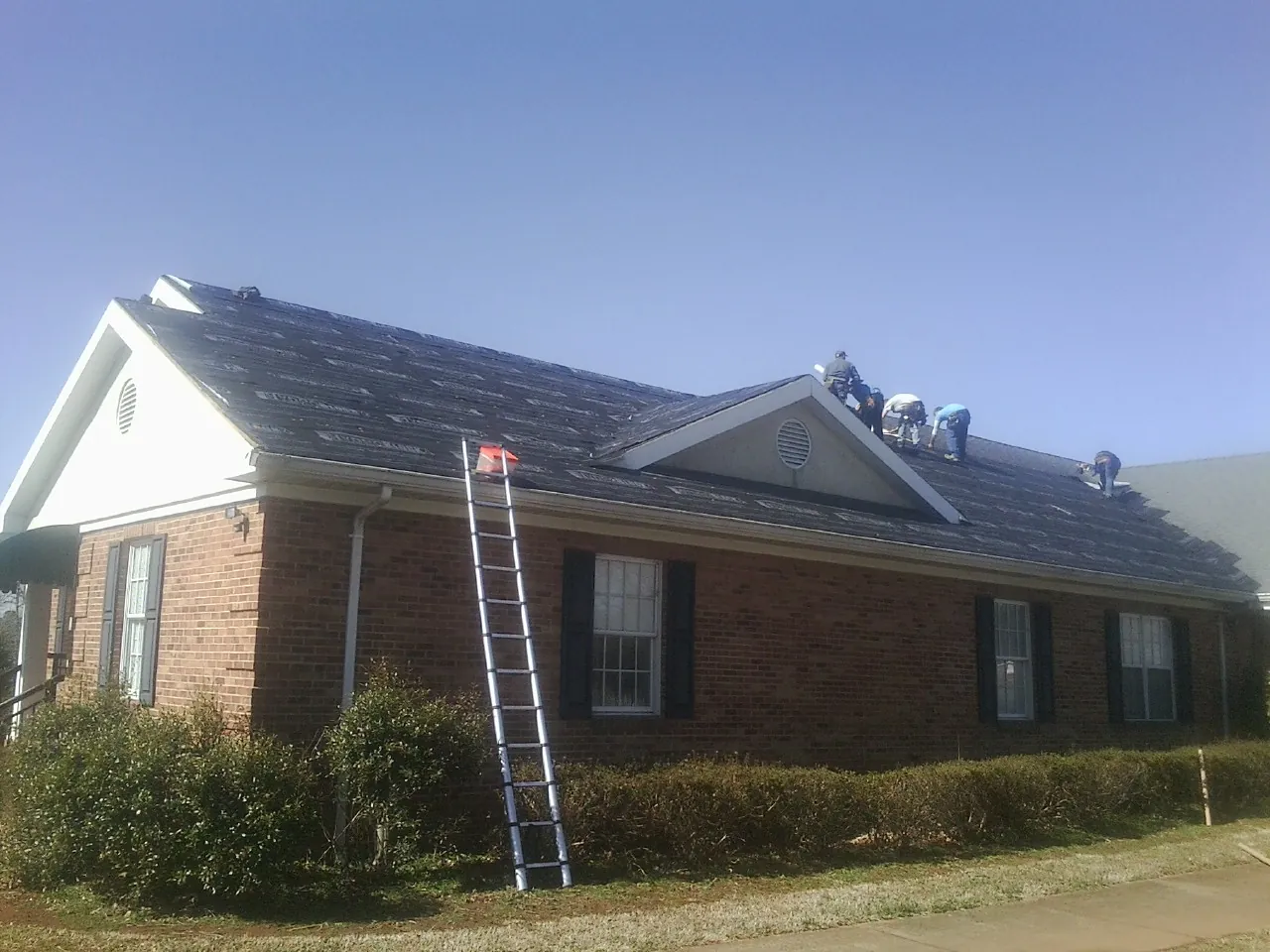Crew tearing shingles off a brick ranch roof with a ladder set — Emergency Roof Repair work by our crew in Hubertus