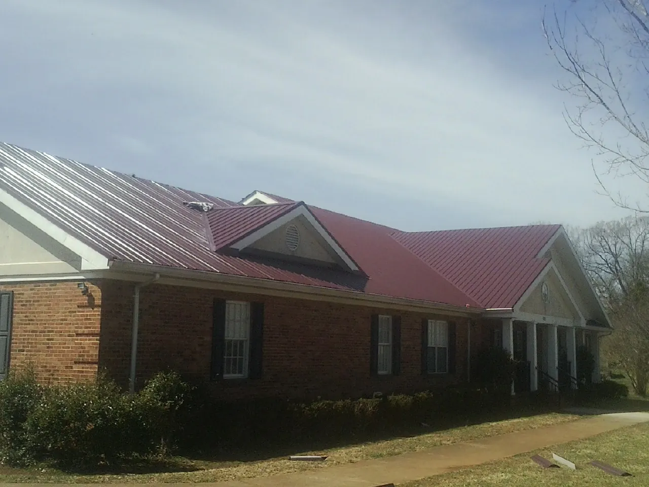 Red metal roof with gabled entries on a long brick building, from a Hail Damage Roof Repair job in Hubertus