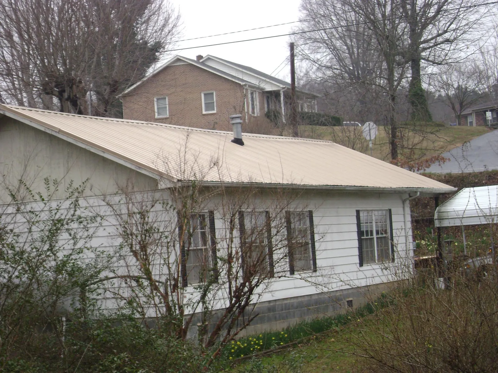 Tan metal roof on a white sided house set into a hillside — Commercial Roofing by Roofing Brothers in Hubertus